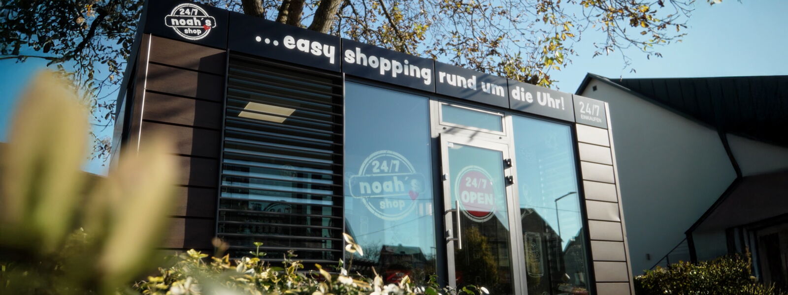 24/7 Selbstbedienungsshop Außenansicht mit Glasfassade und Beschriftung „easy shopping rund um die Uhr“